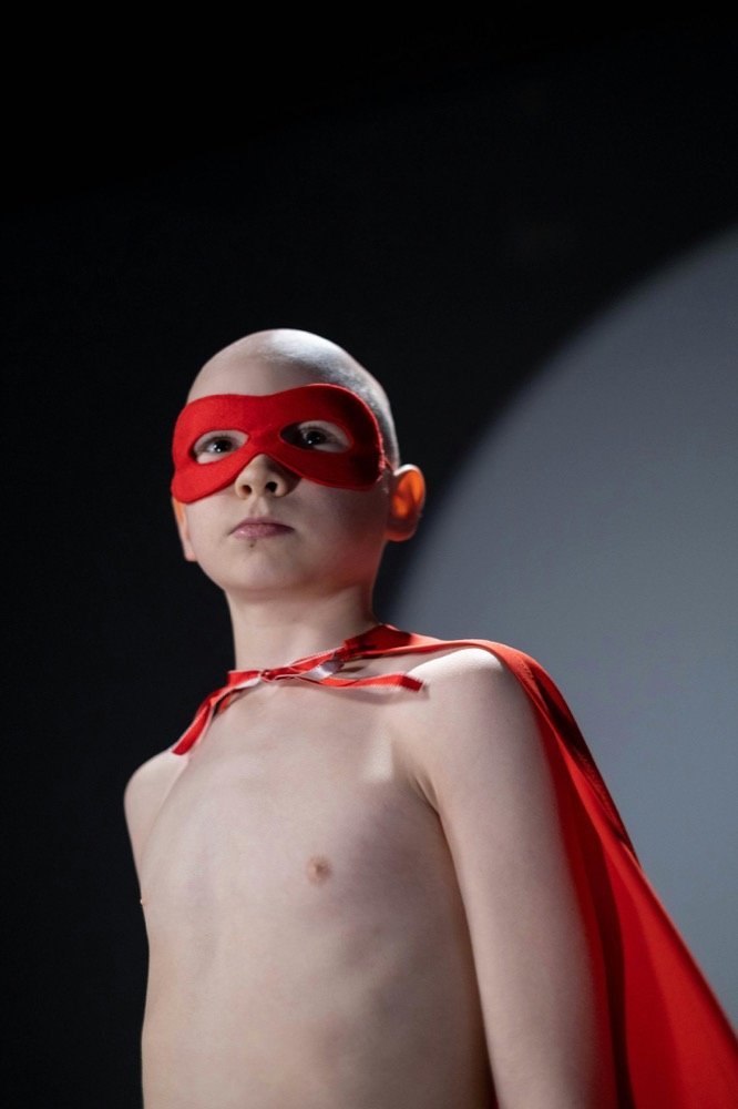 Un enfant portant un masque et une cape rouges de super-héros regarde au loin